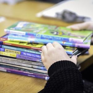 Stock image of a child's hands going through a stack of books on a table