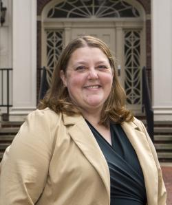 Miller wears a tan jacket and black shirt, smiling at the camera