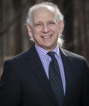 Gene Sasso smiles in front of camera while wearing formal attire