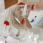 Close-up of a scientist's gloved hand handling a syringe in a lab setting