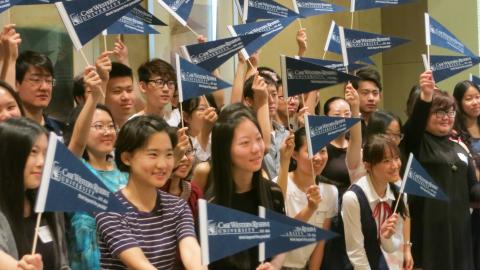 Group of incoming CWRU students, posed and smiling for the camera, waving CWRU pennant flags