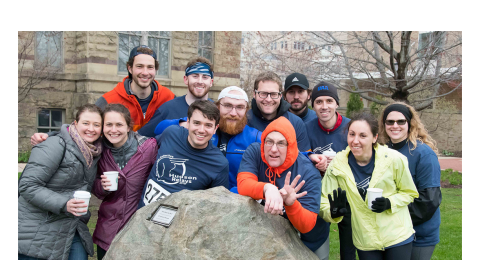 Photo of group of alumni on the 2018 Hudson Relays team, posed and smiling around the rock near Adelbert Hall