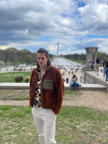 Kyle stands with his hands in his pockets looking at the camera with the Washington Monument in the background