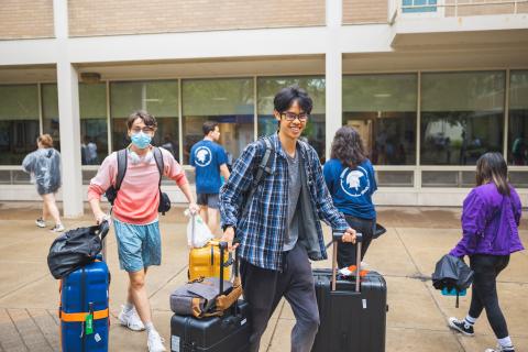Students smile at the camera while they wheel their suitcases in the rain to move into the dorms