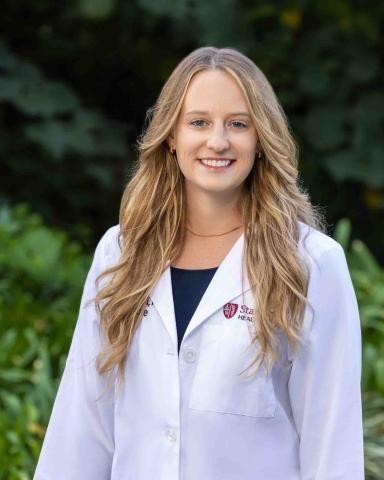 Amber Beserra, outside, wears a white coat with the Stanford Medicine logo on it
