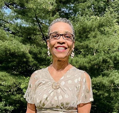 Linda Berry Wheatt smiles at camera in an outdoor setting while wearing a metallic-colored blouse