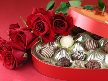 Photo of red roses, laying on top of an open box of assorted chocolates