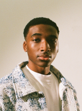 Abdul Seidu poses for camera while wearing a T shirt and collared, textured jacket