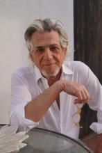 Alan Rosenberg poses for camera at a table, while holding eyeglasses in one hand