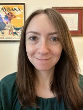 Beth Magid smiles in front of camera with framed images behind her