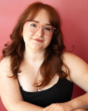 Julia Bianco smiles in front of camera while wearing glasses and a tank top