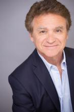 Norman Aladjem smiles in front of camera while wearing formal attire