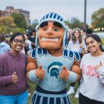 Students and Spartie mascot smile for camera on Freiberger field