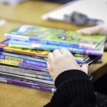 Stock image of a child's hands going through a stack of books on a table