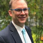 Matthew Garrett smiles at camera while wearing formal attire in an outdoor setting