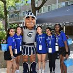 Students smile at camera next to Spartie mascot