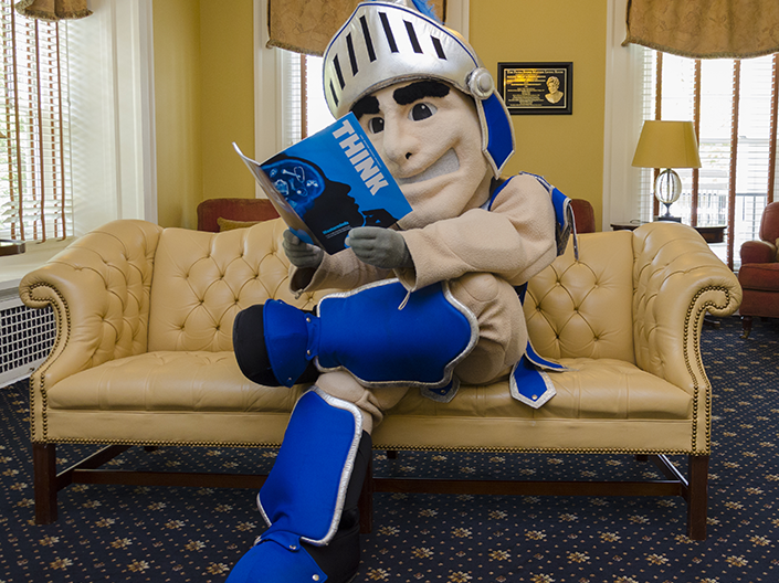 Photo of Spartie, sitting on the couch in the Linsalata Alumni Center, reading Think magazine.