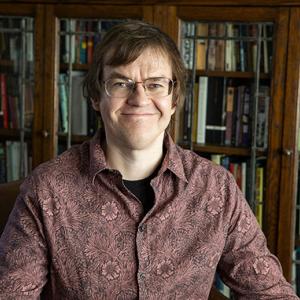 Head shot of white man with glasses wearing a casual shirt in front of book schelf