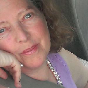 Close up image of older woman with graying hair with face on hand wearing a purple sleeveless top