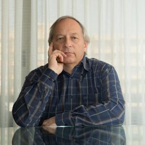 Image of older man in plaid shirt sitting at table with window behind him