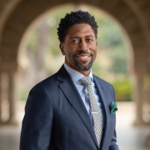 Image of African American man wearing a blue suit and tie outside in front of an archway