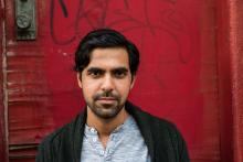 Color image of bearded man wearing a cardigan in front of a red wall