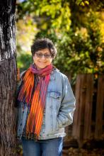 Smiling woman with glasses and a scarf posing by a tree