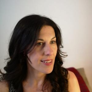 Headshot of white woman with layered shoulder length brown hair in front of a white wall