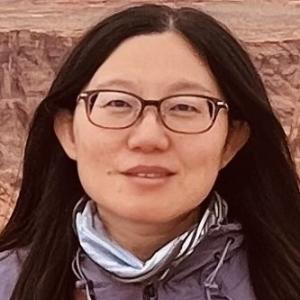 Headshot of Asian woman with long dark hair parted in the middle wearing glasses