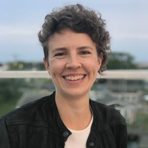 Headshot of smiling white woman with short curly brown hair outside