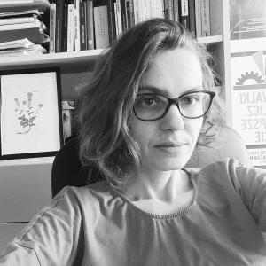 Black and white image of white woman wearing glasses in front of a book shelf