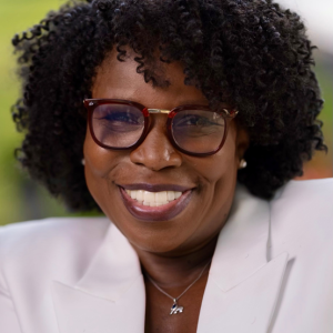Image of smiling African American woman with glasses and short curly hair wearing a white suit jacket