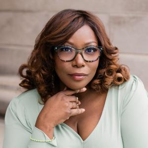 Color image of African American woman wearing a light blue vneck top with shoulder length hair and glasses