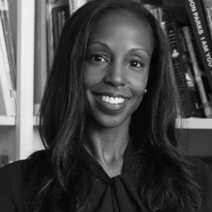 black and white headshot of smiling African American women with long hair sitting in front of a bookcase