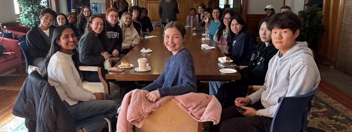 Color image of students sitting around a seminar table with a woman speaking at the head of the table