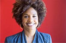 Headshot of smiling African American woman in blue suit with gold hoop earrings in front of a red background