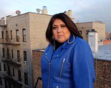 Outdoor photo of dark haired women wearing a blue jacket on the roof of a building