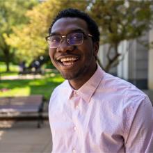 Young African American Man wearing a pink shirt and glasses smiling broadly outside