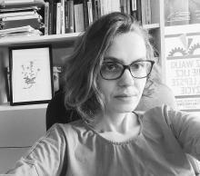 Black and white image of white woman wearing glasses in front of a book shelf