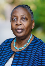 Image of African American woman with her hair pulled back wearing a blue necklace and jacket.