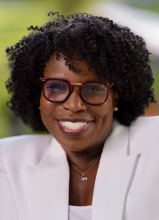 Image of smiling African American woman with glasses and short curly hair wearing a white suit jacket