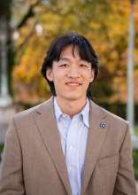 Color outdoor image of smiling young man with dark hair wearing a beige jacket