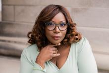 Color image of African American woman wearing a light blue vneck top with shoulder length hair and glasses