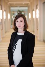 Color photo of woman with shoulder length brown hair wearing a black and white top