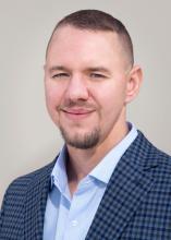 Head shot of white man with very short brown hair wearing blue dress shirt and jacket