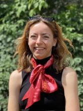 Image of smiling younger woman standing outside in front of tree wearing sleevelss black top with red scarf