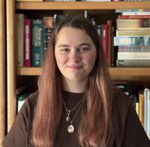 Headshot of young woman with long brown hair in front of a book shelf
