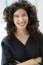 Head shot of smiling woman with dark curly hair and her arms crossed