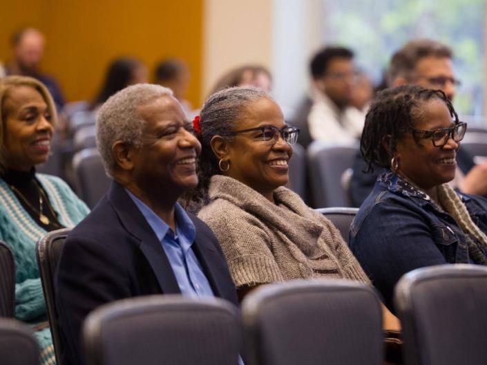 Program participants seated in an auditorium smiling towards the front of the room.