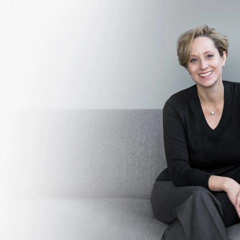 Image of smiling white woman with short brown hair wearing a black sweater sitting on a couch